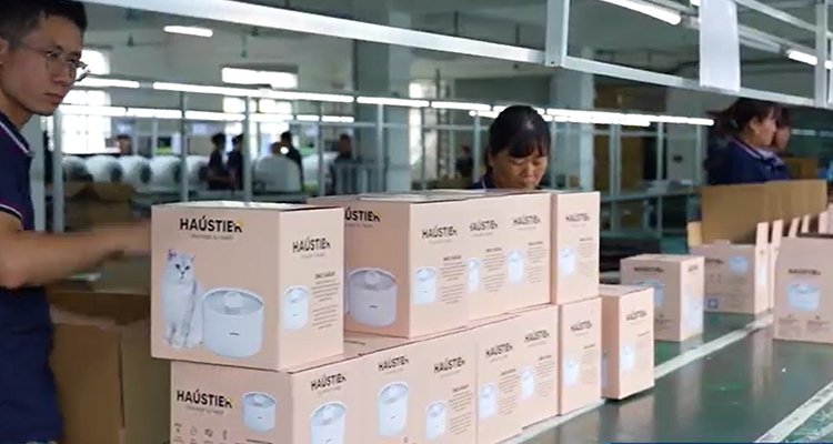Low MOQ Cat Water Fountain Factory in China 2 of Low MOQ Cat Water Fountain Factory in China: Essential Small-Scale Importing Guide 2025 A worker on an assembly line stacking boxes of pet water fountains, showing the packaging and shipping process at a Low MOQ cat water fountain factory in China.
