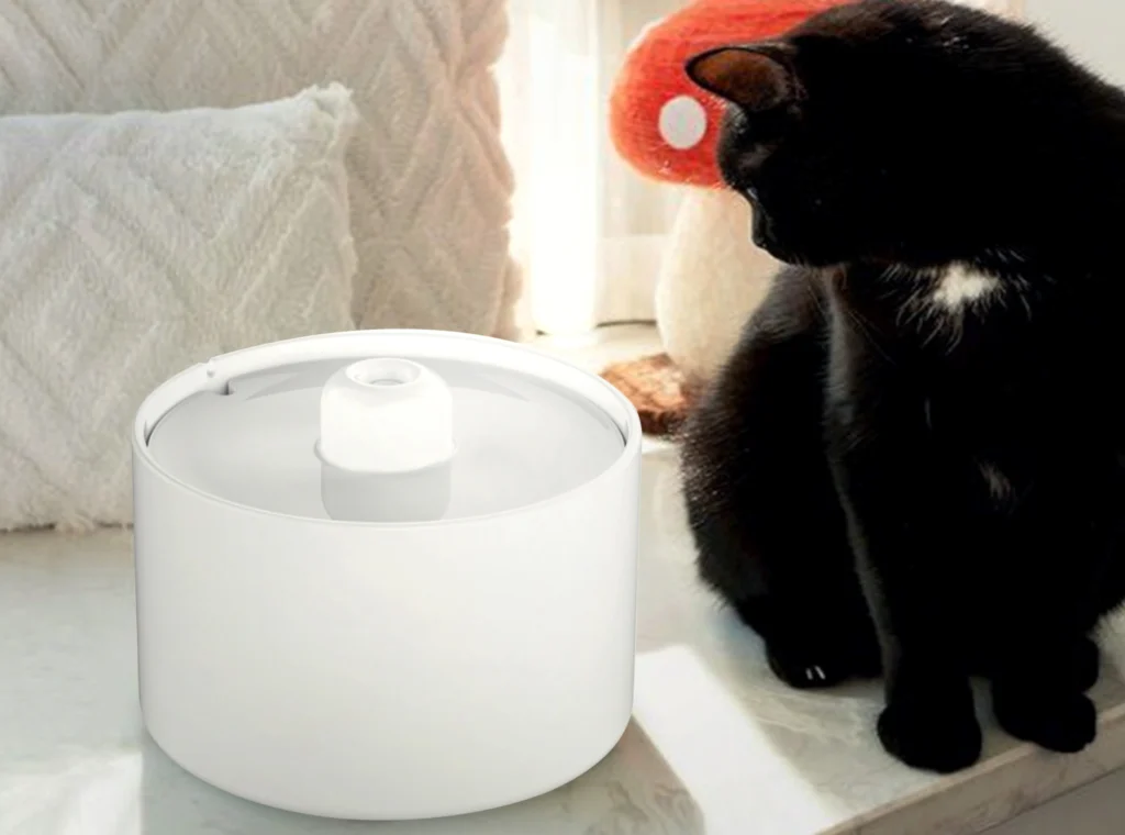 A black cat sits next to a small, white, ceramic-style, minimalist automatic cat water fountain with a glowing spout, showcasing a customer's product design.