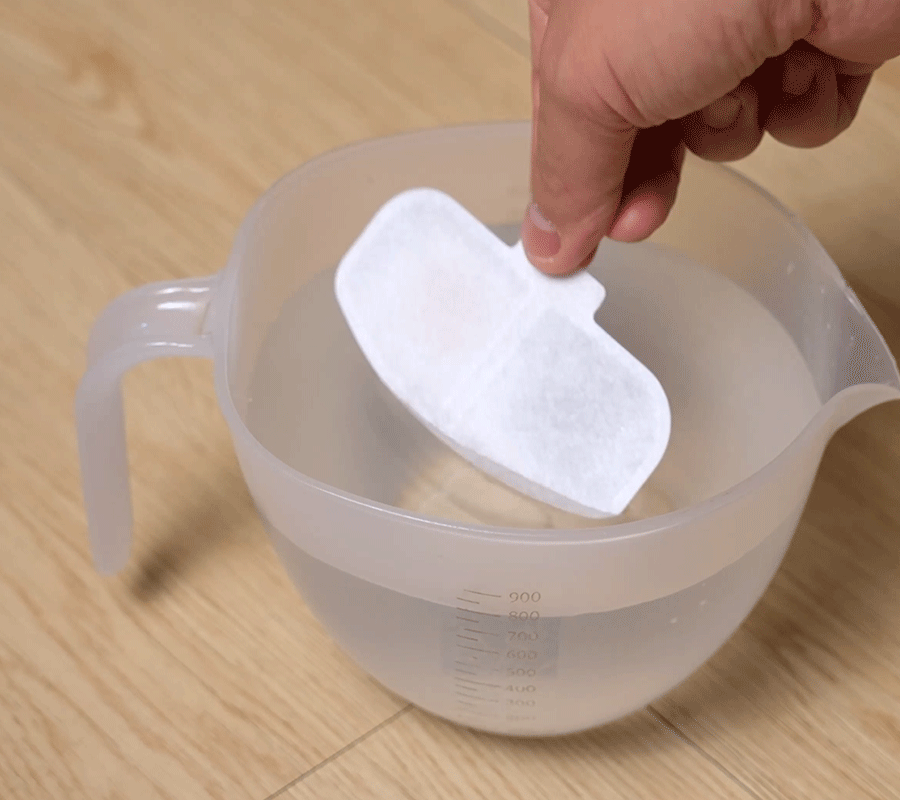 How to Install Use Our Cat Water Fountain Step 1 of Automatic Cat Water Fountain A hand soaking the white filter element in a measuring cup of water, the first step for the automatic cat water fountain setup.