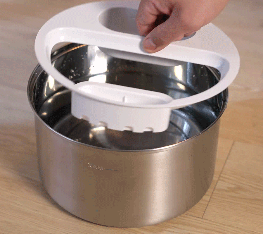 How to Install Use Our Cat Water Fountain Step 3 of Automatic Cat Water Fountain A hand placing the white plastic filter tray assembly into the filled stainless steel base of the automatic cat water fountain.