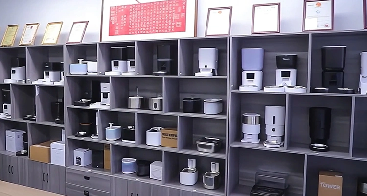 A wall of shelving in a showroom filled with dozens of various models of smart pet feeders and water fountains, representing the extensive product range being prepared for MEGAZOO 2025 Korea.
